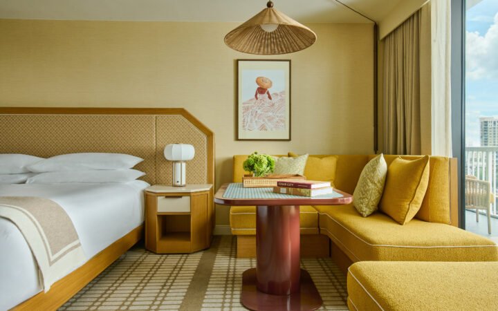 Hotel Cala guestroom with a bed, mustard-yellow corner seating and balcony window.