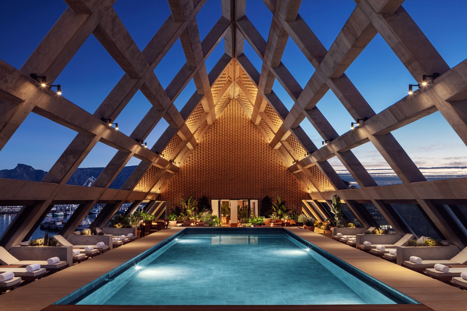 Cape Town EDITION rooftop pool beneath exposed structural beams at dusk.