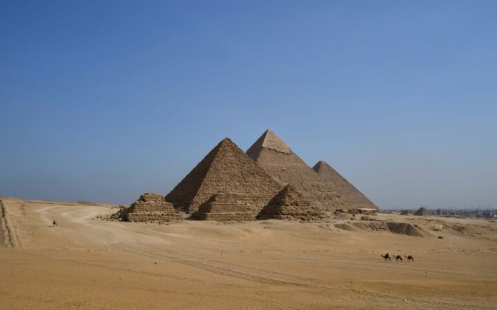 The Pyramids of Giza rising above the Egyptian desert, with camels in the foreground.