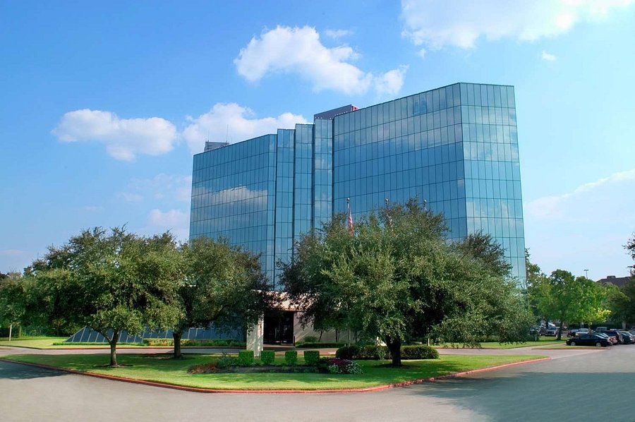 Hilton Houston Westchase exterior with glass-fronted towers, trees and entrance driveway